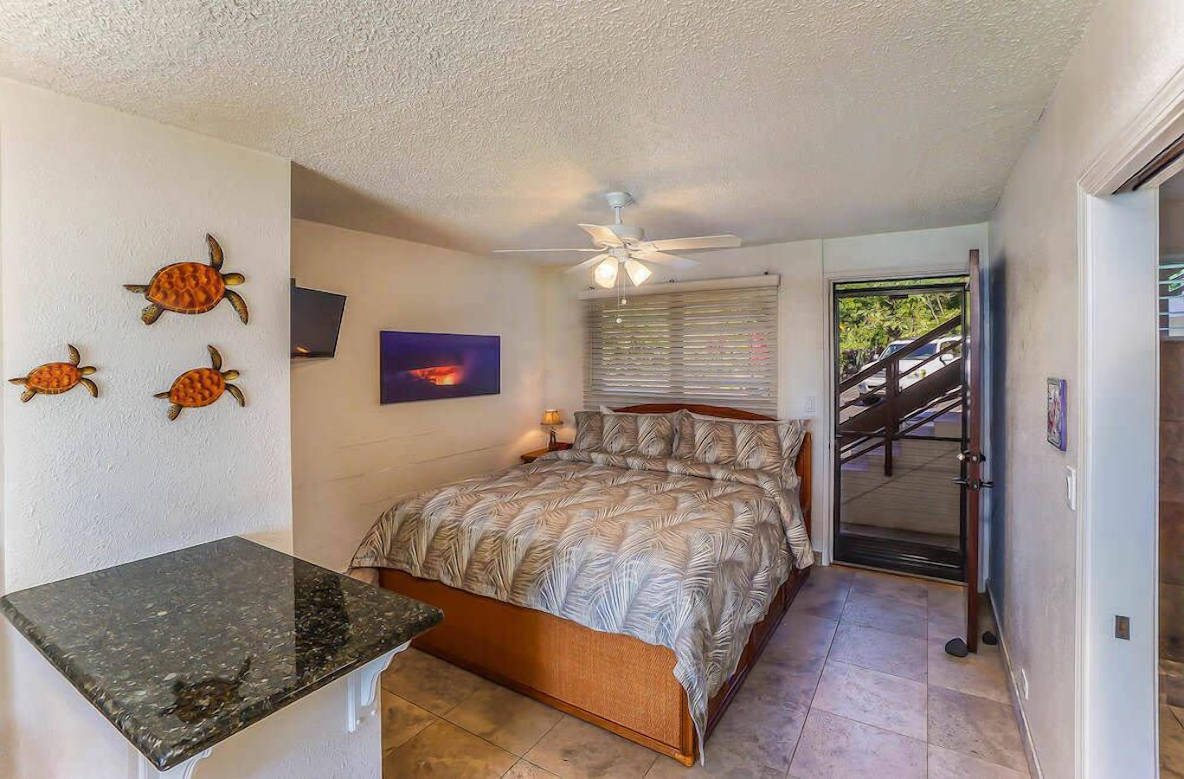 A bedroom with a bed, a ceiling fan, a window with blinds, and a view of a staircase leading outside.