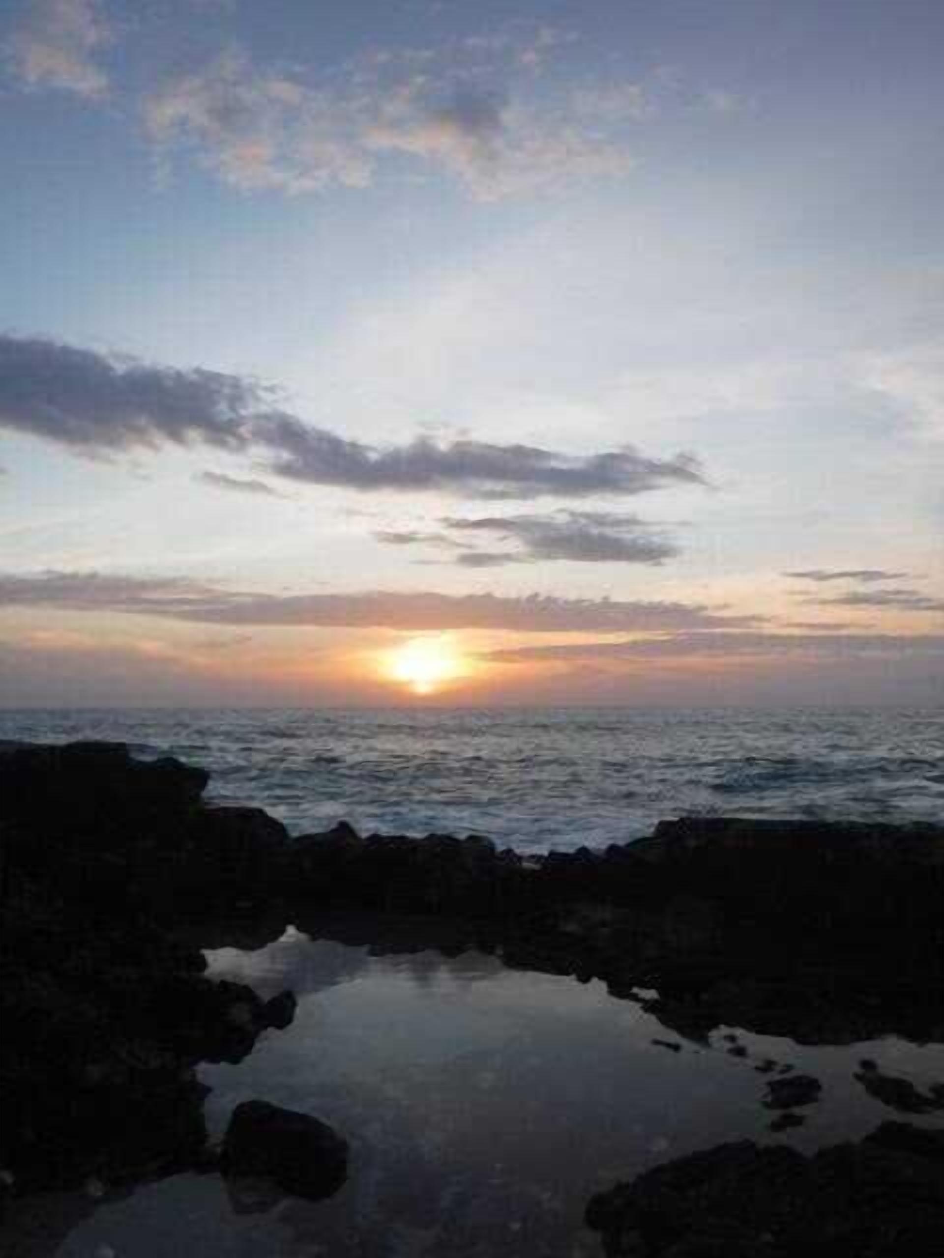 A sunset over the ocean with a rocky shoreline in the foreground.