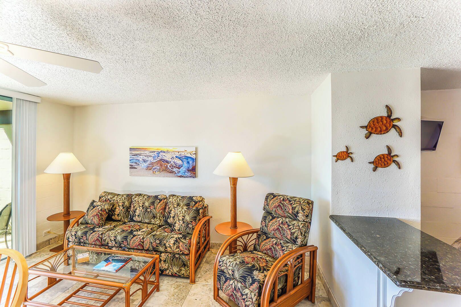 A living room with a sofa, armchairs, a coffee table, and a painting of a beach scene. There are two lamps and a wall-mounted turtle decoration.
