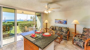 A kitchen with a view of the ocean, a ceiling fan, and a dining area with a sofa and chairs. - Kona White Sands A4 Romantic Ocean View! (Kailua-Kona)