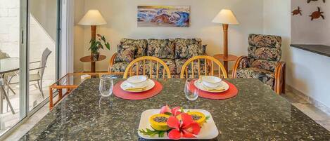 Un comedor con una mesa de mármol, sillas y un cuadro con temática tropical en la pared.