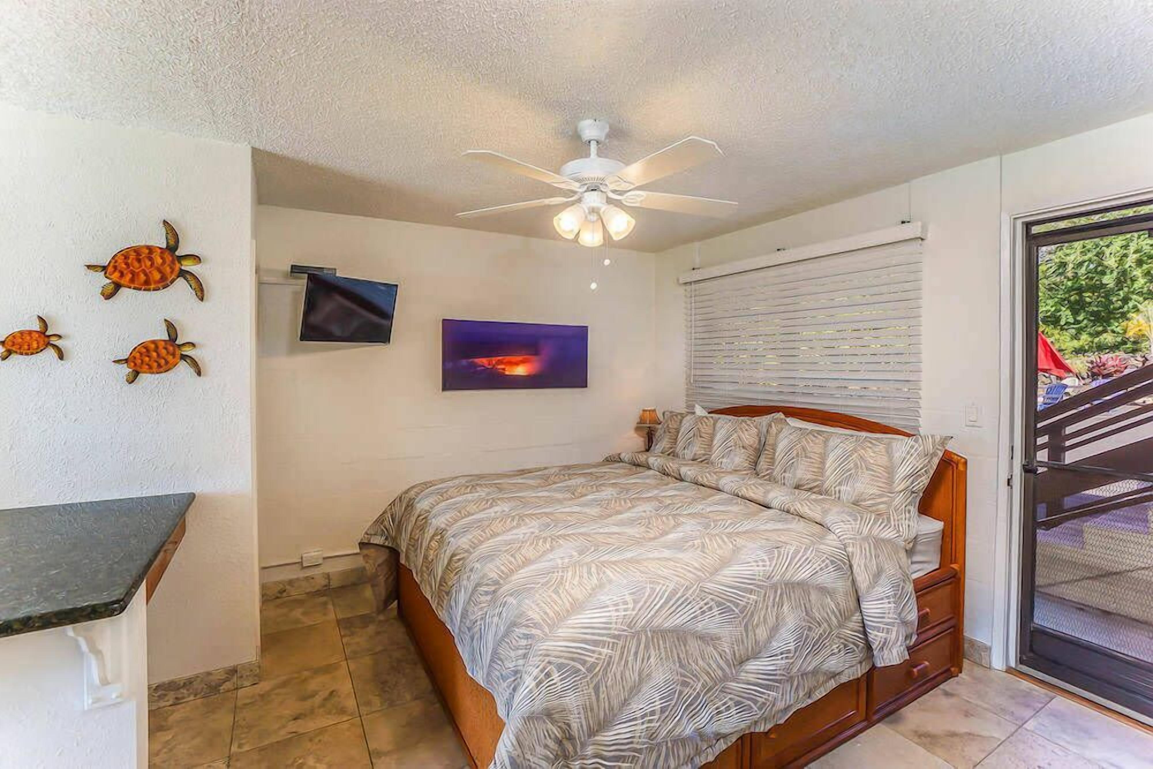 A bedroom with a bed, a ceiling fan, a TV, and a window with blinds.