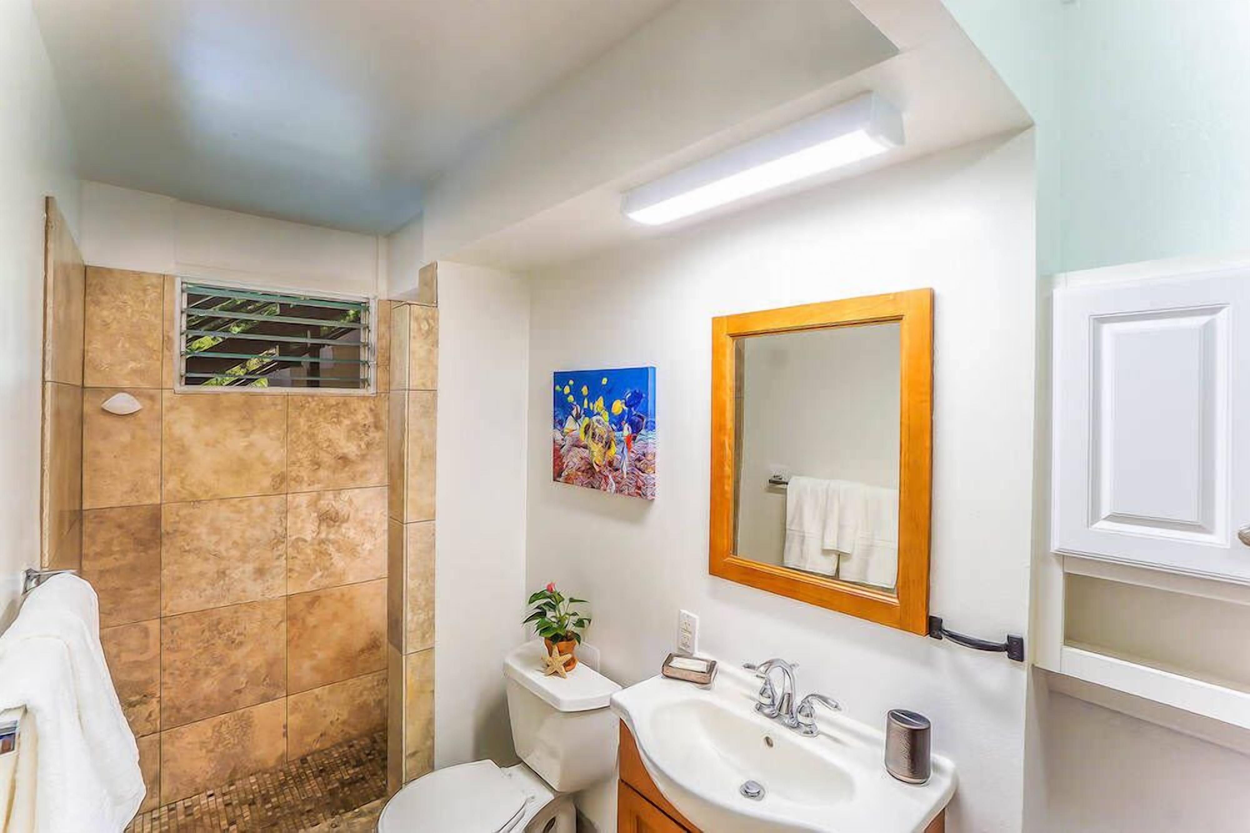 A bathroom with a shower, toilet, sink, and a mirror with a wooden frame.