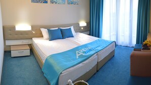A hotel room with a bed, a nightstand, a table with a bottle, and a chair. - Arena Mar Hotel & SPA - All Inclusive (Varna)