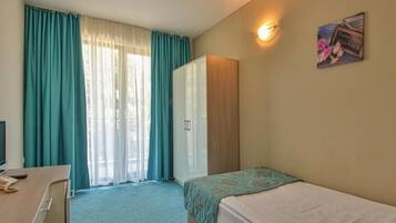 Quarto de hotel com cama, escrivaninha, guarda-roupa e janela com cortinas.