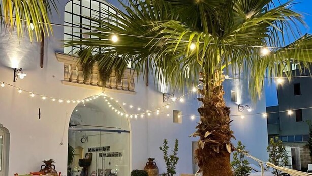 An outdoor seating area with string lights, palm trees, and a building with a glass facade. - Rural mansion from the 1700s with swimming pool, hot tub and solarium. (Nardò)