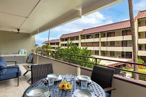 Un balcó amb taula preparada per dinar, envoltat de cadires de vimet i vista cap a un edifici amb diversos balcons.