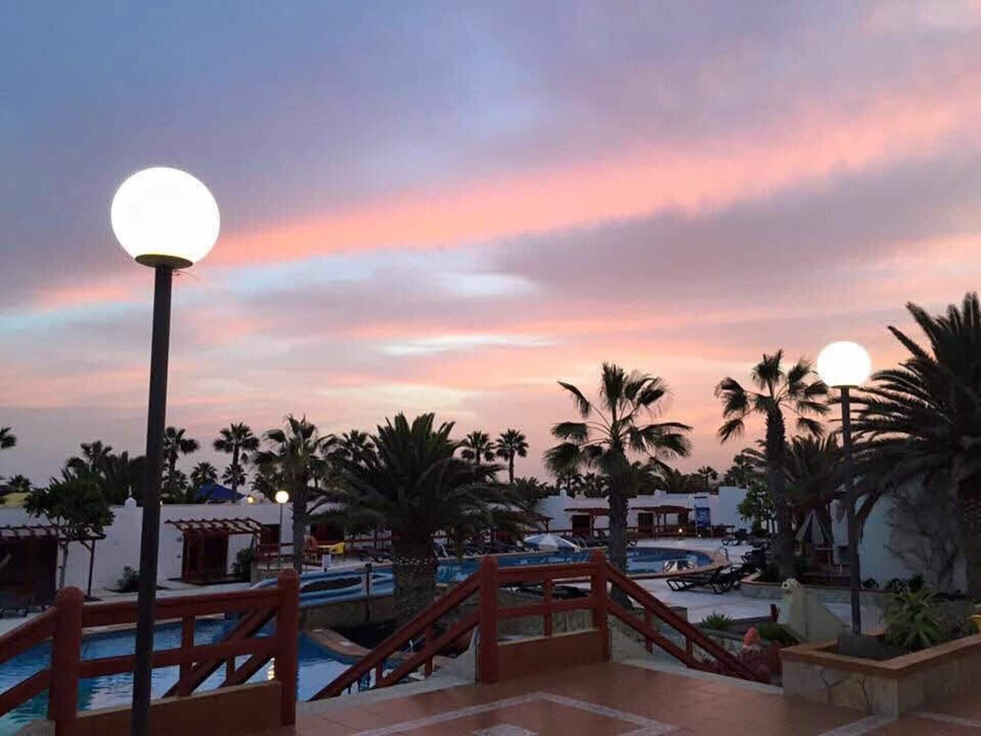 A resort with a pool, palm trees, and a sunset sky.