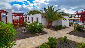 Un patio con un camino de piedra, paredes blancas y una pérgola roja.
