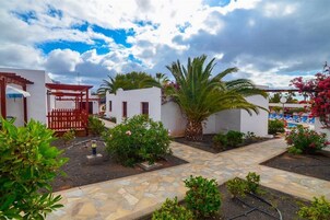 Un patio con un camino de piedra, paredes blancas y una pérgola roja.