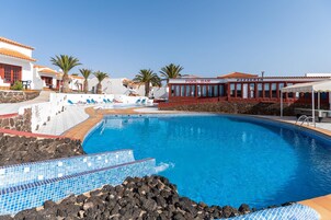 Una piscina rodeada de edificios blancos, un bar junto a la piscina y una pizzería.