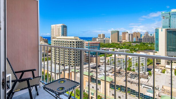 A balcony with a view of a cityscape, including high-rise buildings and a body of water.