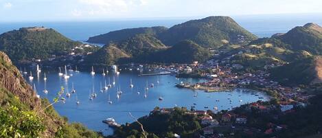 Un pueblo costero con un puerto deportivo lleno de barcos, rodeado de colinas y vegetación.