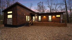 Een houten chalet met een stenen fundering, een overdekt terras en een trap naar de ingang.