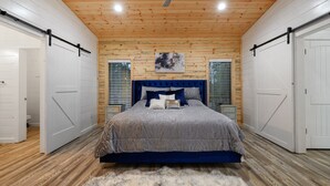 Een slaapkamer met een groot bed, houten plafond, witte muren en een houten vloer.