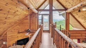 A wooden interior with a high ceiling, a central staircase, and a view of the outdoors. - Sky Views - 2BR/New Hot Tub/New Firepit/Grill/Sleeps 8 (Gatlinburg)