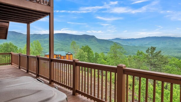 A wooden deck with a view of green mountains and a clear sky. - Sky Views - 2BR/New Hot Tub/New Firepit/Grill/Sleeps 8 (Gatlinburg)