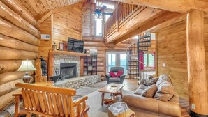A log cabin interior with a fireplace, wooden furniture, and a staircase leading to an upper level. - Sky Views - 2BR/New Hot Tub/New Firepit/Grill/Sleeps 8 (Gatlinburg)