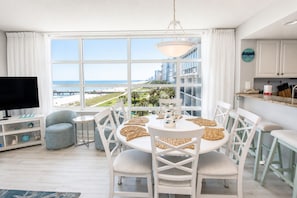 A modern kitchen with white cabinets, a dining area with a round table, and a view of the beach.