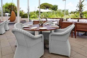 An outdoor dining area with wicker chairs and tables, surrounded by greenery and a white umbrella. - La Suite Hotel Spa X (Procida)