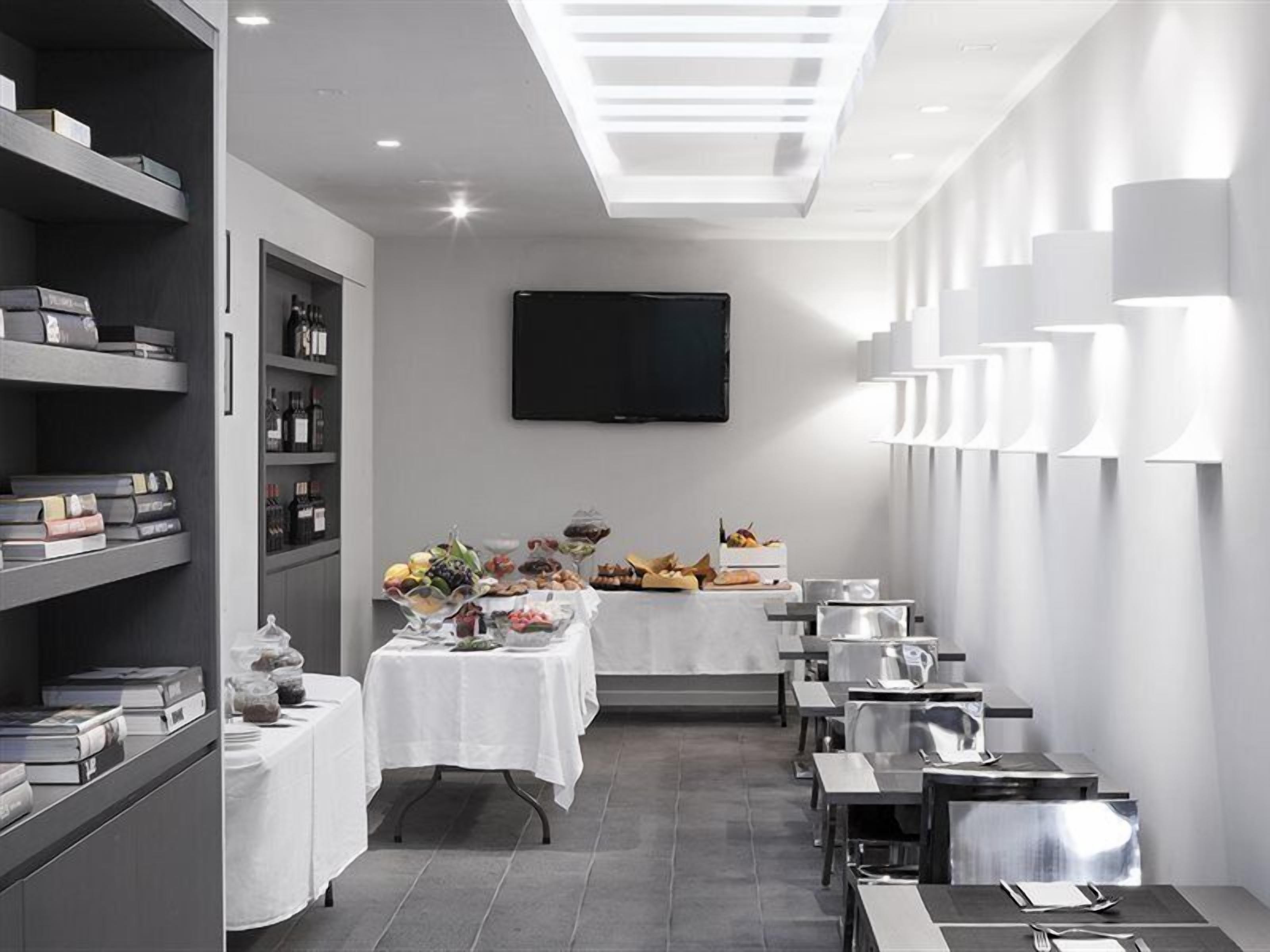 A modern dining area with a long table set for a meal, a television mounted on the wall, and a row of tall, white lamps along the wall.
