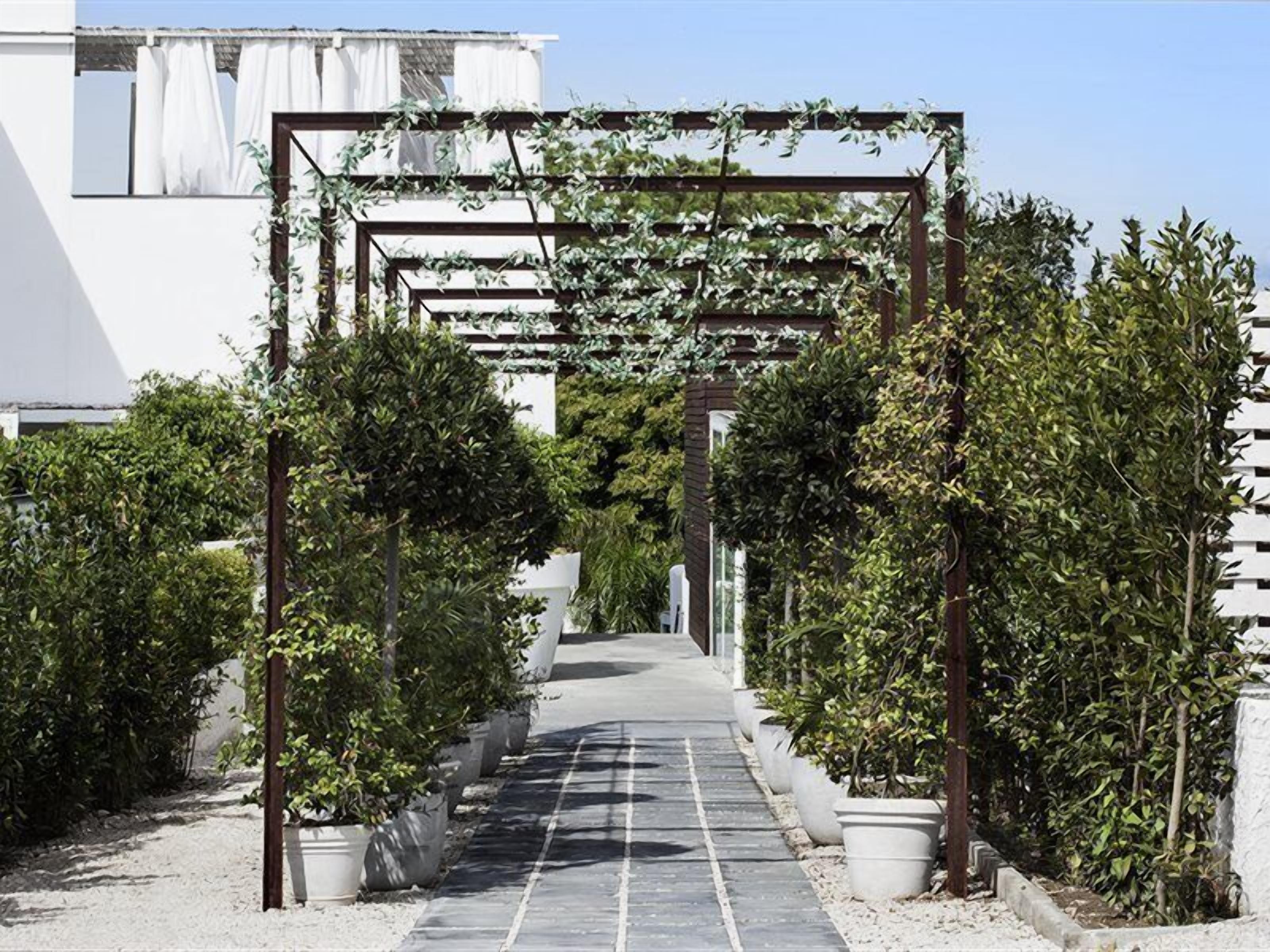 A pathway lined with potted plants and a pergola structure.
