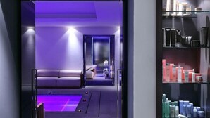 Um spa moderno com área de relaxamento iluminada em roxo, um espelho e prateleiras com diversos produtos de higiene pessoal.