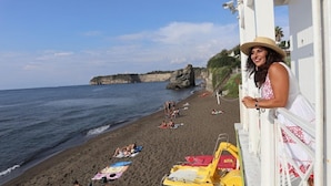 Uma praia com pessoas se banhando ao sol, um penhasco rochoso ao fundo e um edifício com fachada branca.