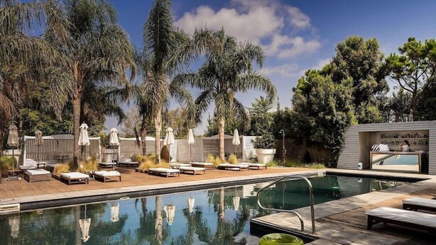 Área de piscina com espreguiçadeiras, guarda-sóis e um bar com uma grande janela.