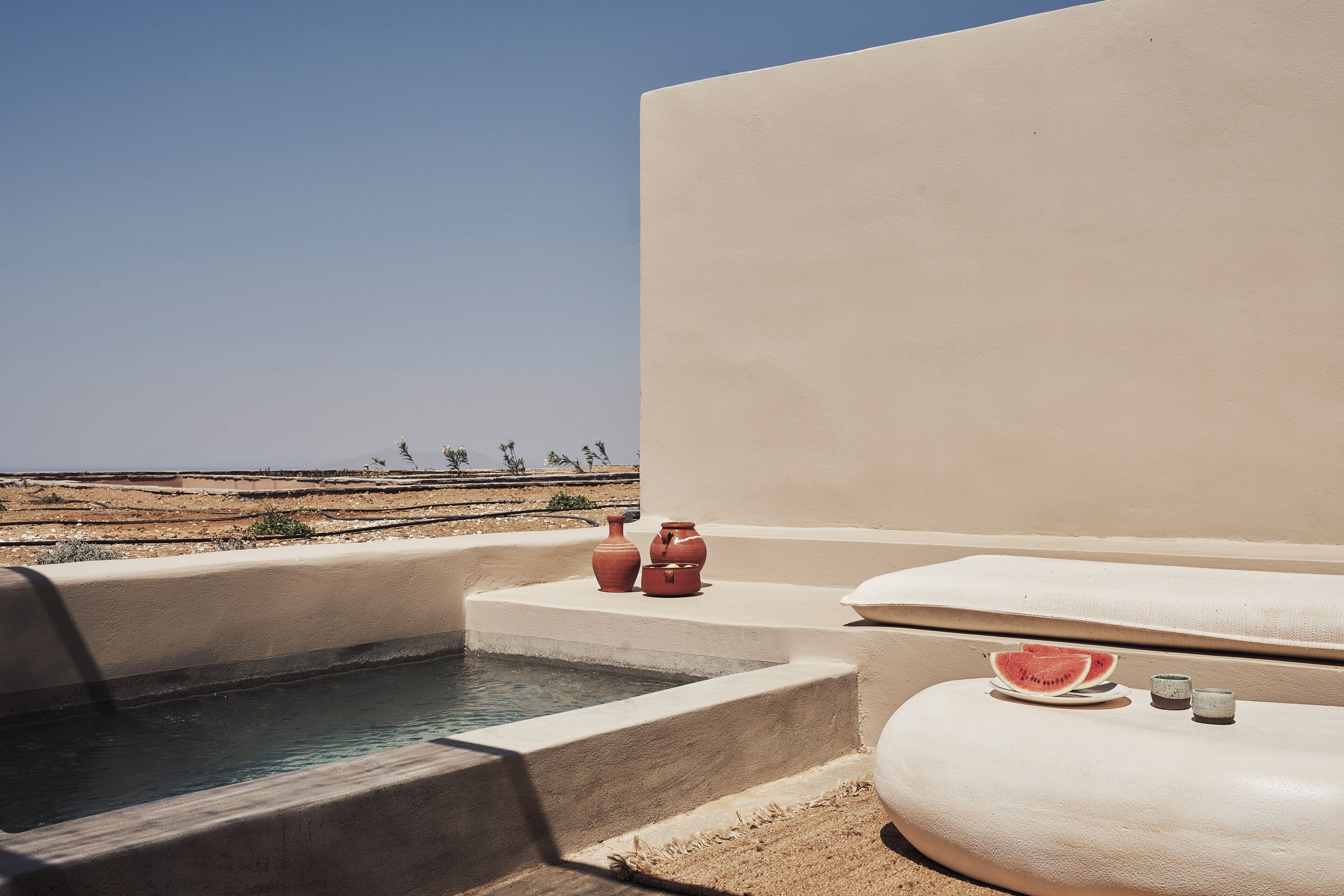 A pool area with a view of the desert, a hot tub, and a small table with a watermelon slice.