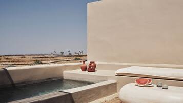 A pool area with a view of the desert, a hot tub, and a small table with a watermelon slice.
