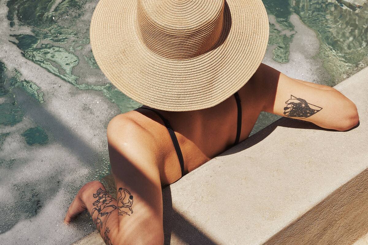 A person relaxing in a clear pool with visible water patterns, wearing a straw hat and black bikini.