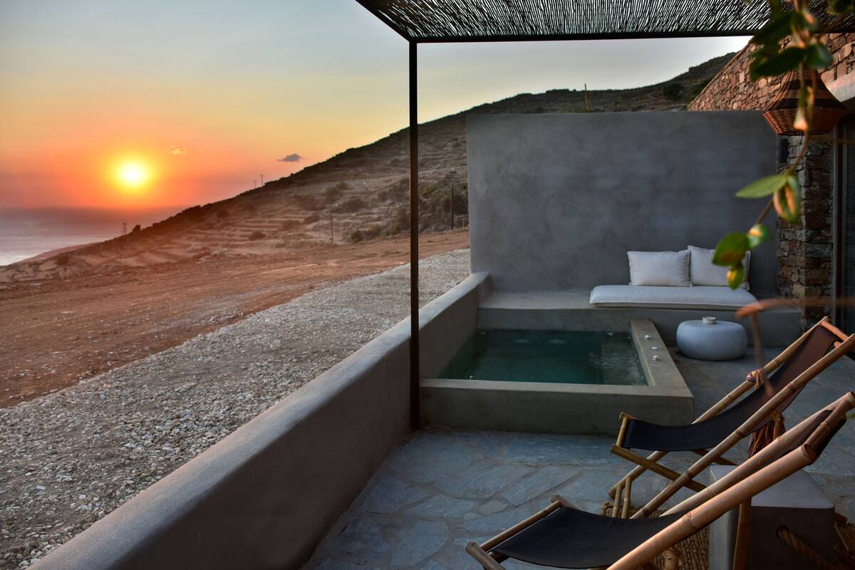 A rooftop terrace with a hot tub, lounge chairs, and a view of the sunset over the sea.