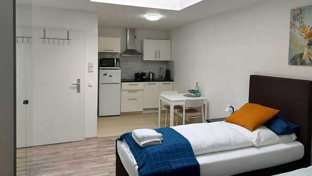 A modern hotel room with a bed, a small desk, a kitchenette, and a skylight. - Studio Apartment 30m2 (Bad Homburg vor der Höhe)