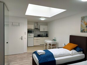 A modern hotel room with a bed, a small desk, a kitchenette, and a skylight.