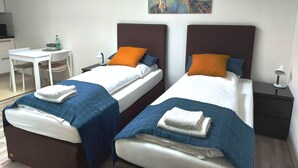 A hotel room with two beds, a desk, and a painting on the wall. - Studio Apartment 30m2 (Bad Homburg vor der Höhe)
