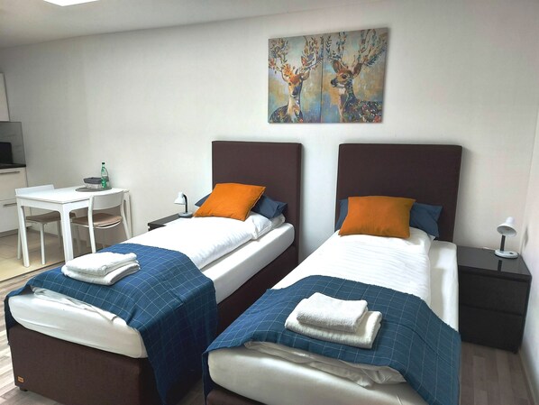 A hotel room with two beds, a desk, and a painting on the wall.