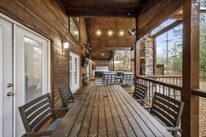 Una terraza de madera con chimenea de piedra, mobiliario exterior y vistas del bosque circundante.