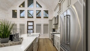 Una cocina moderna con un refrigerador de acero inoxidable grande, piso de madera y un ventanal sobre el fregadero.