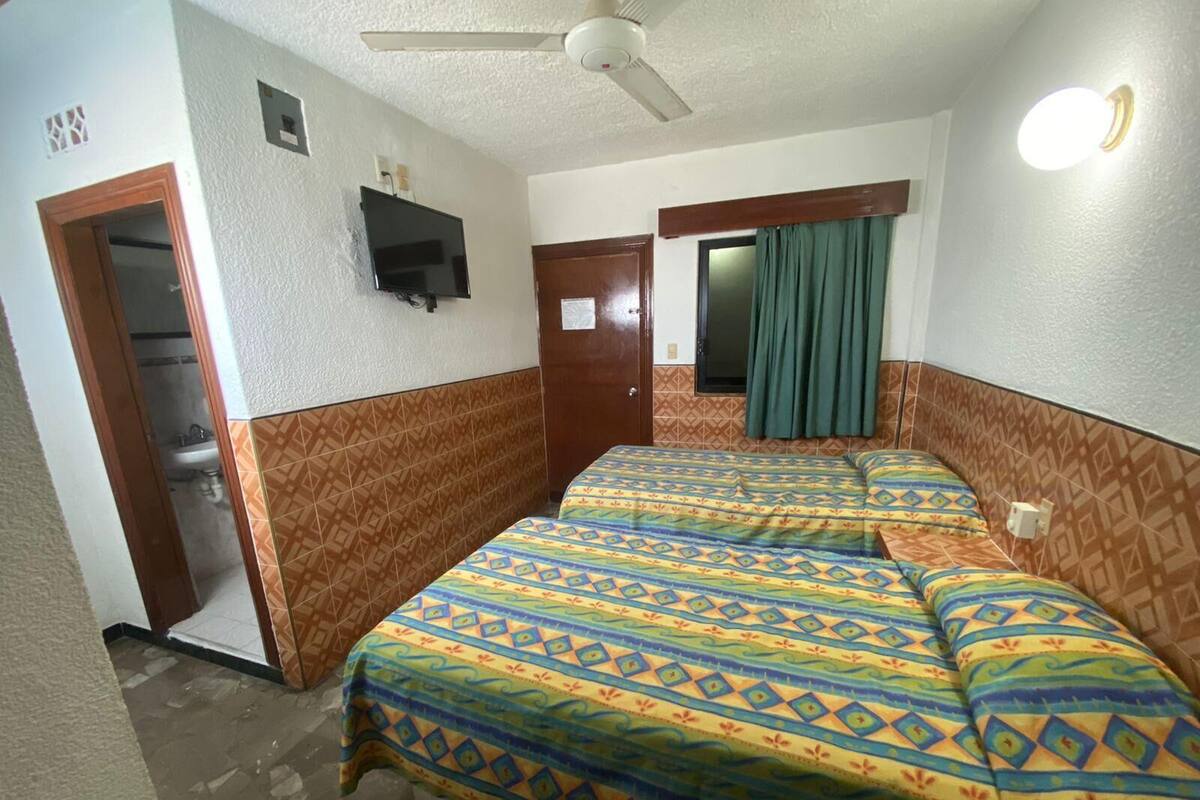 A hotel room with two beds, a ceiling fan, a TV, and a bathroom visible through an open door.