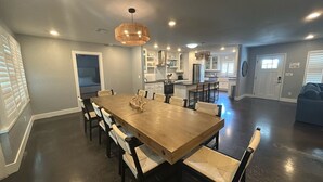 A spacious dining area with a wooden table and chairs, a kitchen in the background, and a modern ceiling light fixture. - Private Heated Pool, walk to St Armand's! Perfect for families! (Lido Key)