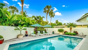 A swimming pool with lounge chairs and umbrellas, surrounded by palm trees and potted plants. - Private Heated Pool, walk to St Armand's! Perfect for families! (Lido Key)