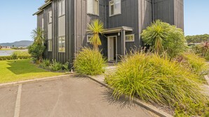 A modern two-story building with a curved facade, large windows, and a well-maintained garden with various plants.
