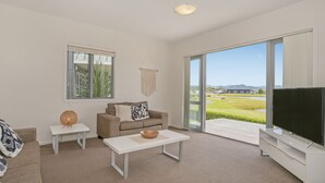 A modern living room with a sofa, coffee table, and TV, featuring a large sliding glass door to a scenic outdoor area.
