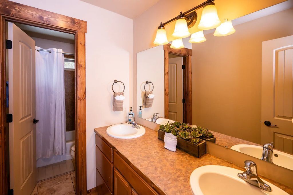 Un baño con dos lavamanos, un espejo grande y una ducha visible a través de una puerta abierta.