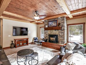 A cozy living room with a stone fireplace, a ceiling fan, a TV, and a comfortable seating area. - Wonderful 5 bdrm cabin on 1acre wooded lot with stream (McCall)