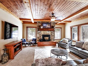 The bright living room has lots of windows, big screen TV and pellet stove