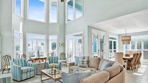 A spacious living room with high ceilings, large windows, and a view of the outdoors. - Beachside 10 | Gorgeous OBA Beach Home! Pool, Grills, Tennis, 500' Beach! (Orange Beach)