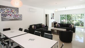 A modern living room with a dining area, featuring a large window, black sofas, and a white table. - Luxury Modern Villa with 6 Bedrooms featuring a Private Pool, Garden, Parking & SPA (Calvi)