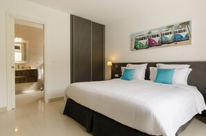 A hotel room with a large bed, a dark headboard, a painting of colorful vans on the wall, and a bathroom visible through an open door.